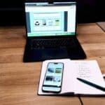 Laptop, iPhone mit der neuen Startseite und ein Notizbuch mit der Liste der sechs Themenwelten auf einem Holztisch